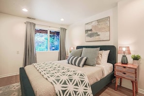 Une chambre à coucher avec un lit, une fenêtre avec des rideaux, une lampe de chevet et un tableau accroché au mur.