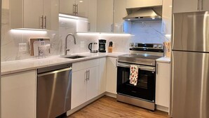 A modern kitchen with stainless steel appliances, white cabinetry, and under-cabinet lighting. - Serene Mercer Island 3B Lower Unit near LR station (Mercer Island)