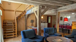 A rustic interior with wooden beams, a staircase, and blue upholstered chairs around a wooden coffee table. - Cozy Countryside Cottage with Spacious Garden – Sleeps 4-5 (Douchy-Montcorbon-Douchy)