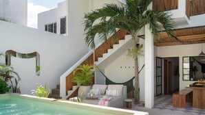 A modern outdoor pool area with a staircase leading to a covered seating area, surrounded by plants and a dining table. - Amazing Villa in la Veleta 14 pax (Tulum)