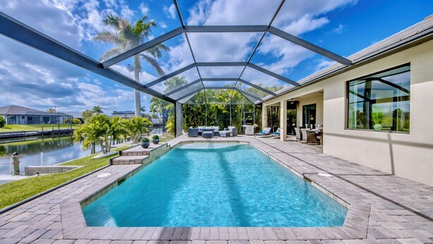 Ein überdachter Pool mit Terrassenbereich, Blick auf das Wasser und ein Gebäude mit großen Fenstern.