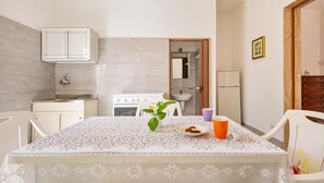 A small kitchen with a table set for two, a white cabinet, a sink, and a stove. - 3052 A Casa di Mario - Appartamento Sabbia by Barbarhouse (Porto Cesareo)