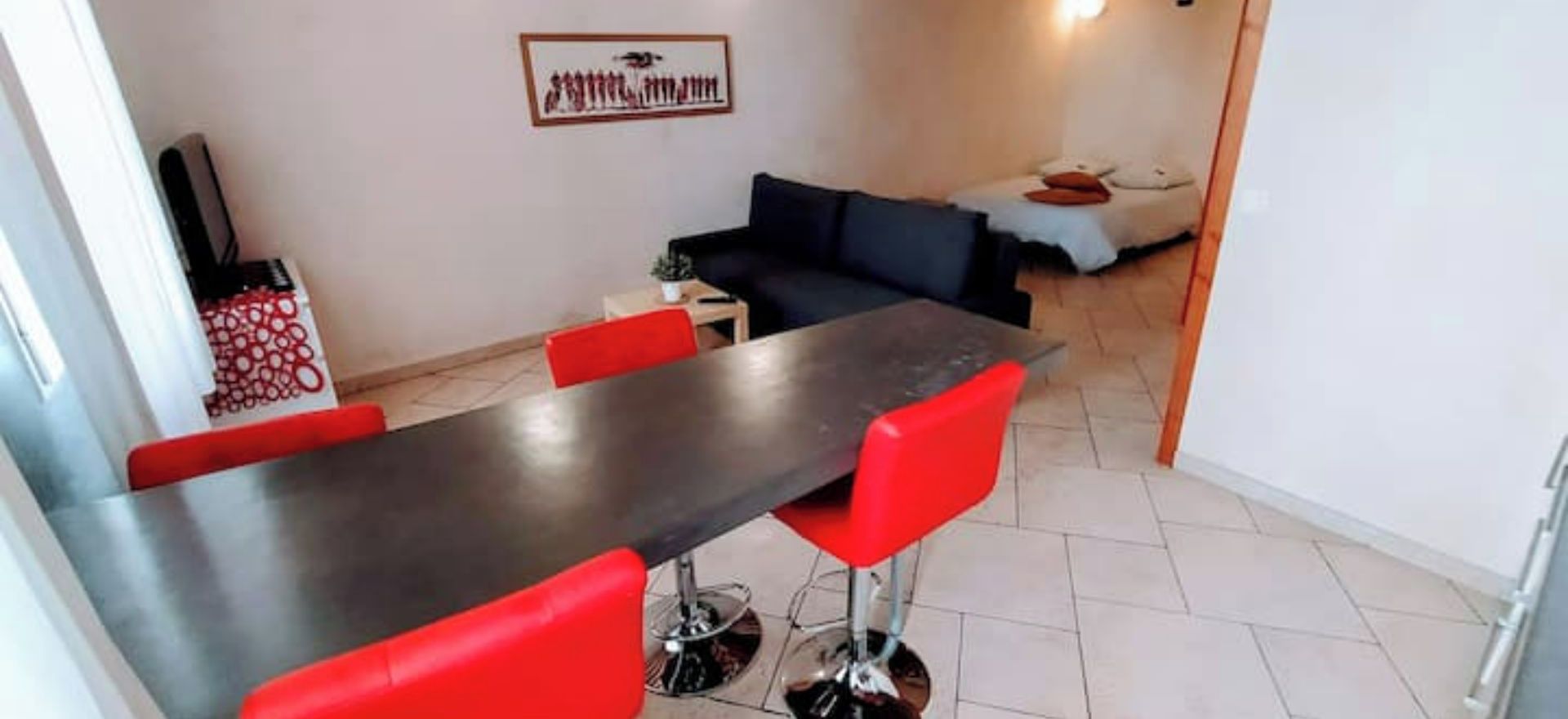 A dining area with a long table and red chairs, a black sofa, and a small side table with a plant.