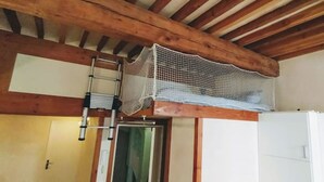 Een kamer met houten balken in het plafond, een witte koelkast en een ladder die tegen de muur staat.