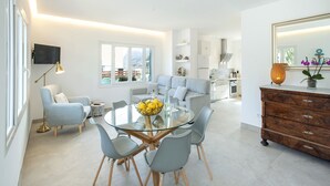 Un salon moderne avec une table à manger en verre, des chaises grises, un canapé et un coin cuisine à l’arrière-plan.