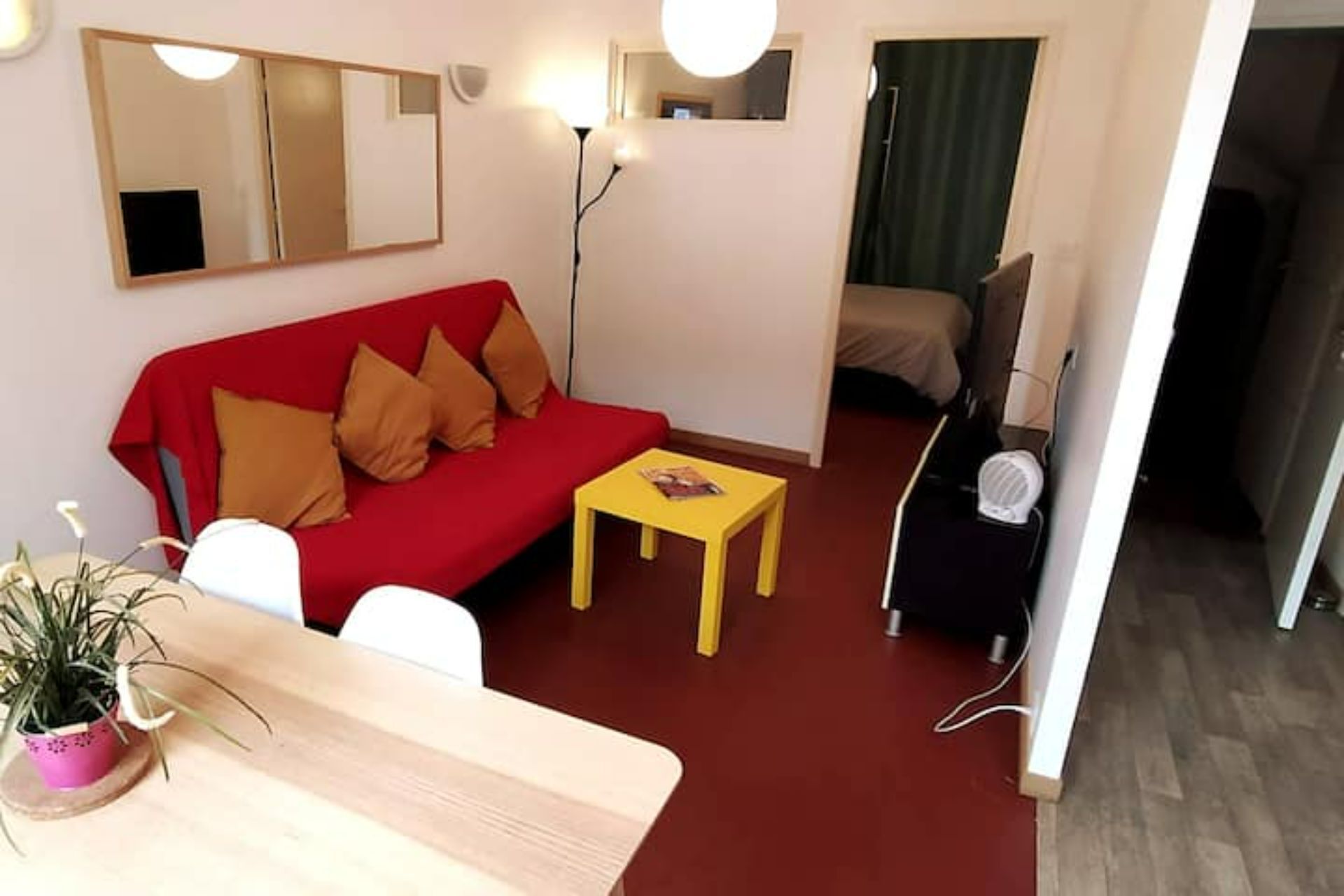 A living room with a red sofa, a small yellow table, and a potted plant.