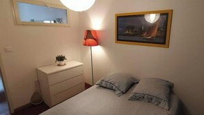 Un dormitori amb un llit, una taula de nit, una làmpada, un quadre i una finestra.