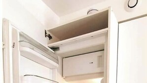 Cuina compacta amb nevera integrat, un rentapeus i armaris blancs.