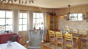 Ein gemütliches Zimmer mit Holzvertäfelung, einem Esstisch mit Stühlen, einem grauen Sessel und einer Vitrine mit Glastüren.