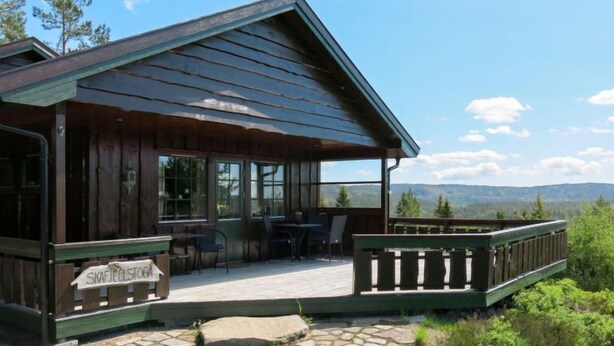 Eine Holzhütte mit überdachter Veranda, Steinböden und einem Schild mit der Aufschrift "SKAFJELSTOGA".