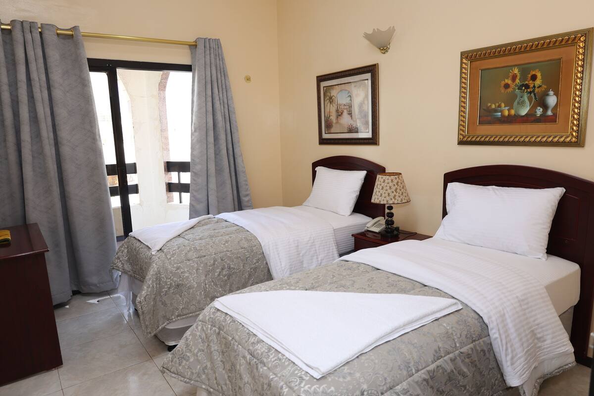 A hotel room with two beds, a desk, a telephone, and a painting on the wall.