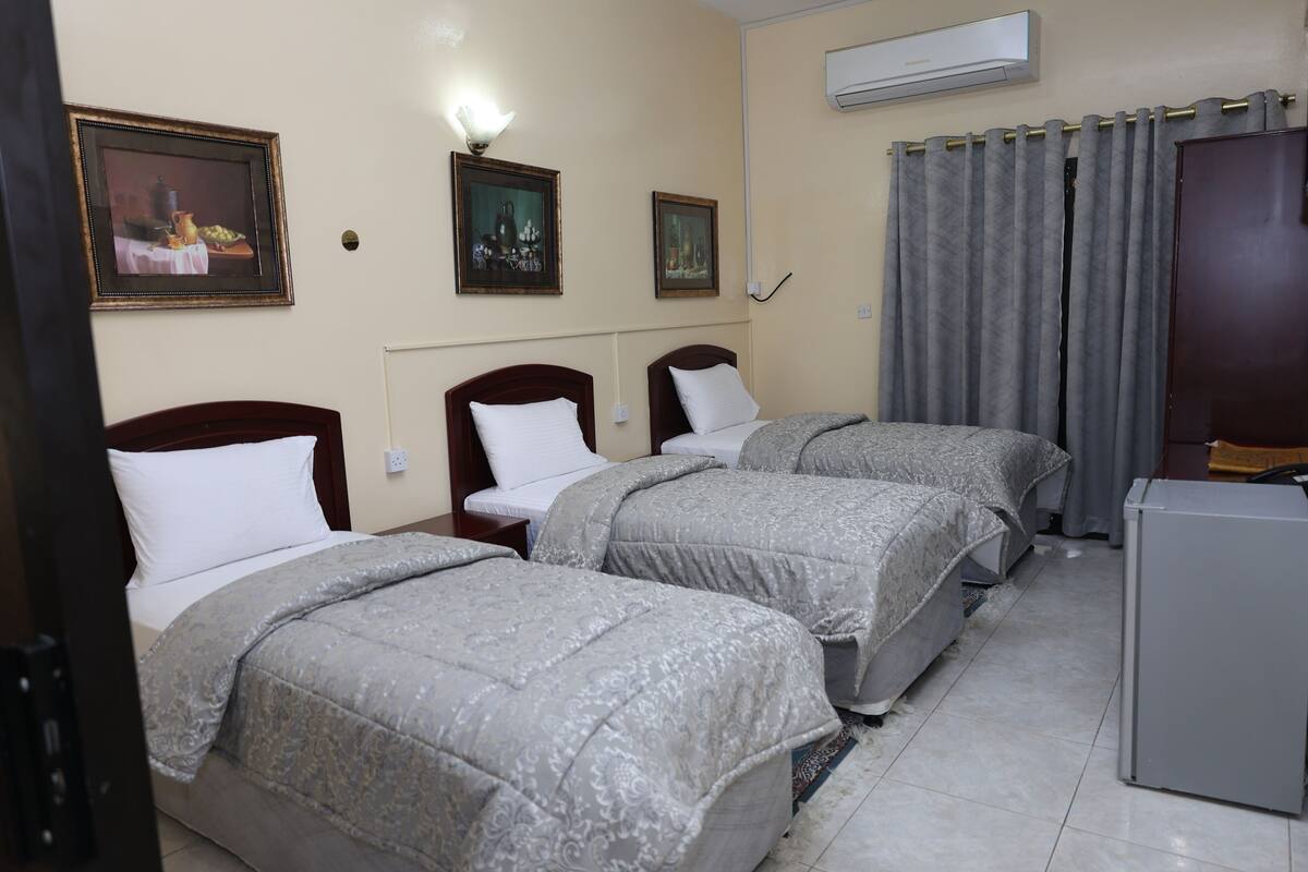 A hotel room with two single beds, a small desk, a refrigerator, and a wall-mounted air conditioner.