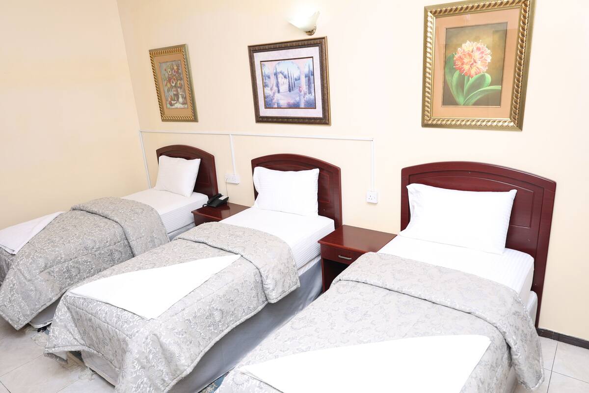 A hotel room with two single beds, a bedside table with a lamp, and three framed pictures on the wall.