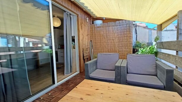 En patio med en skydedør, der fører til et rum, fletmøbler og et træbord.