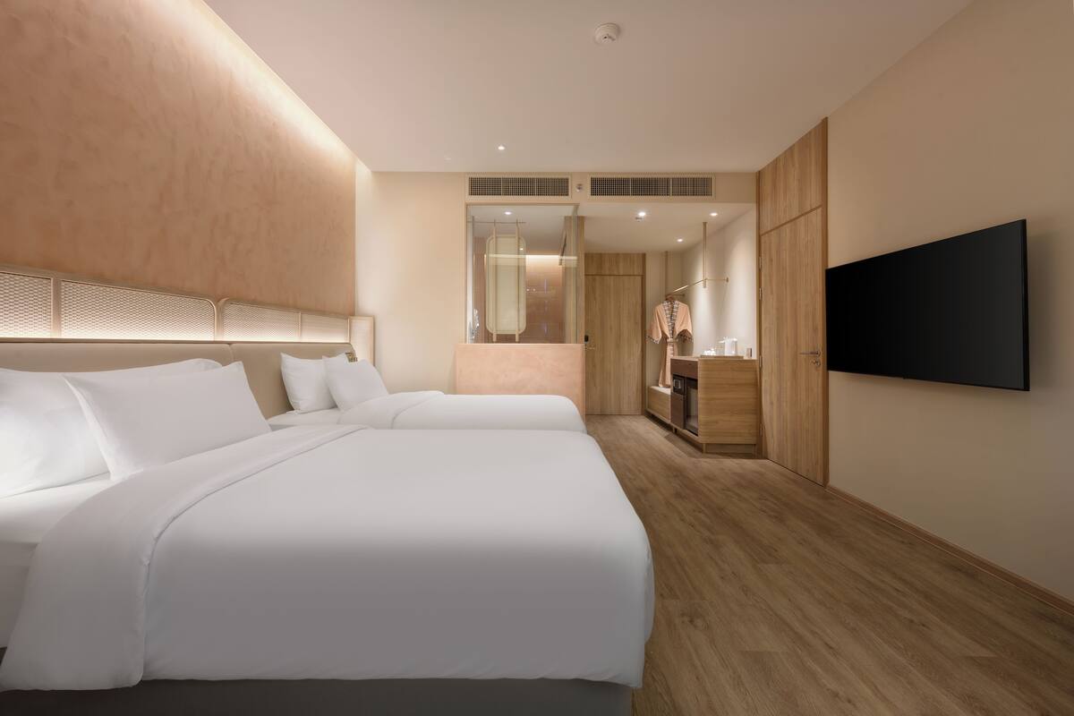 Habitación de hotel con dos camas, televisión, espejo y suelo de madera.