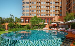 A modern hotel with a large pool featuring mosaic tiles, surrounded by lush greenery and outdoor seating areas.