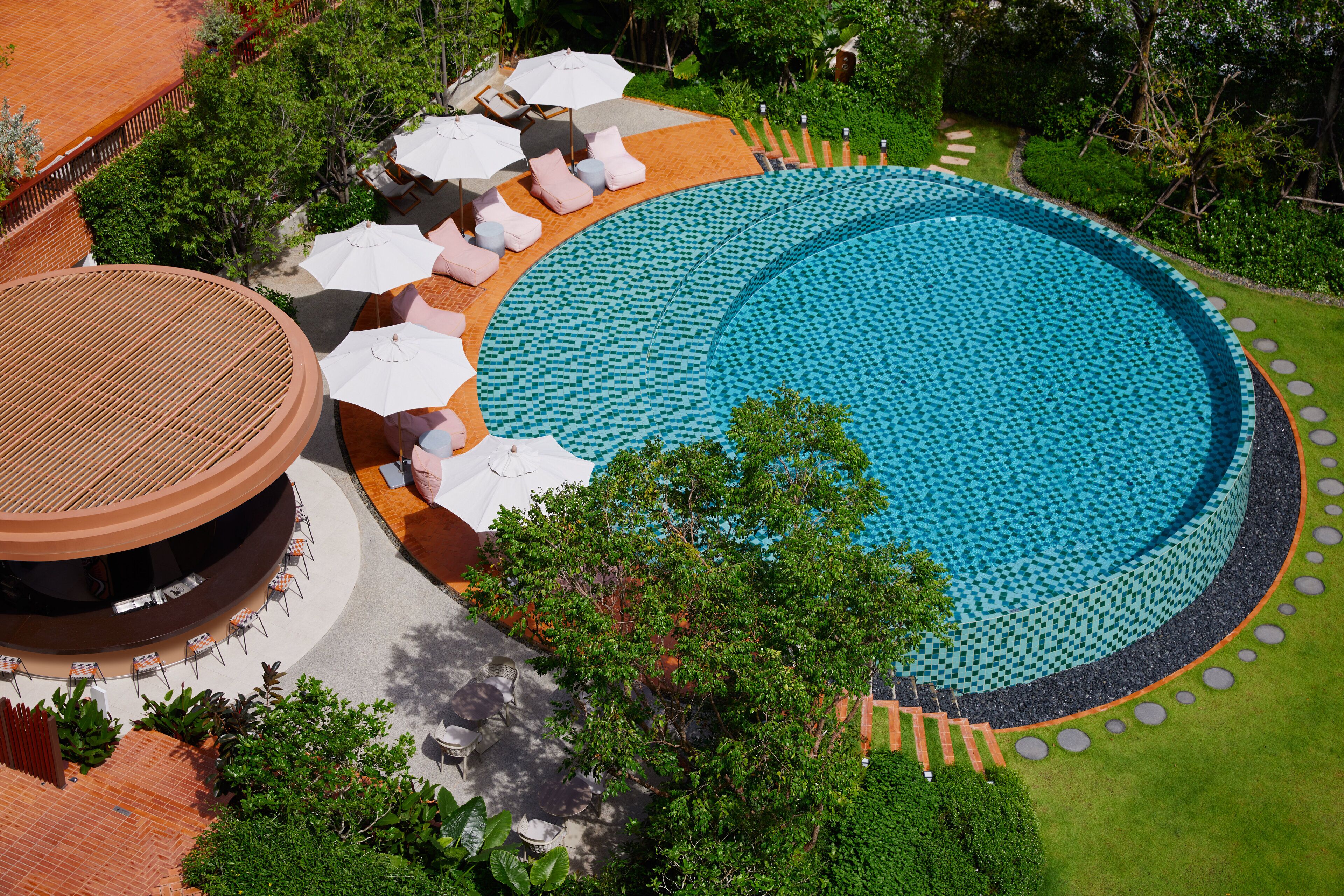 A large circular pool with a tiled edge, surrounded by lounge chairs and umbrellas.