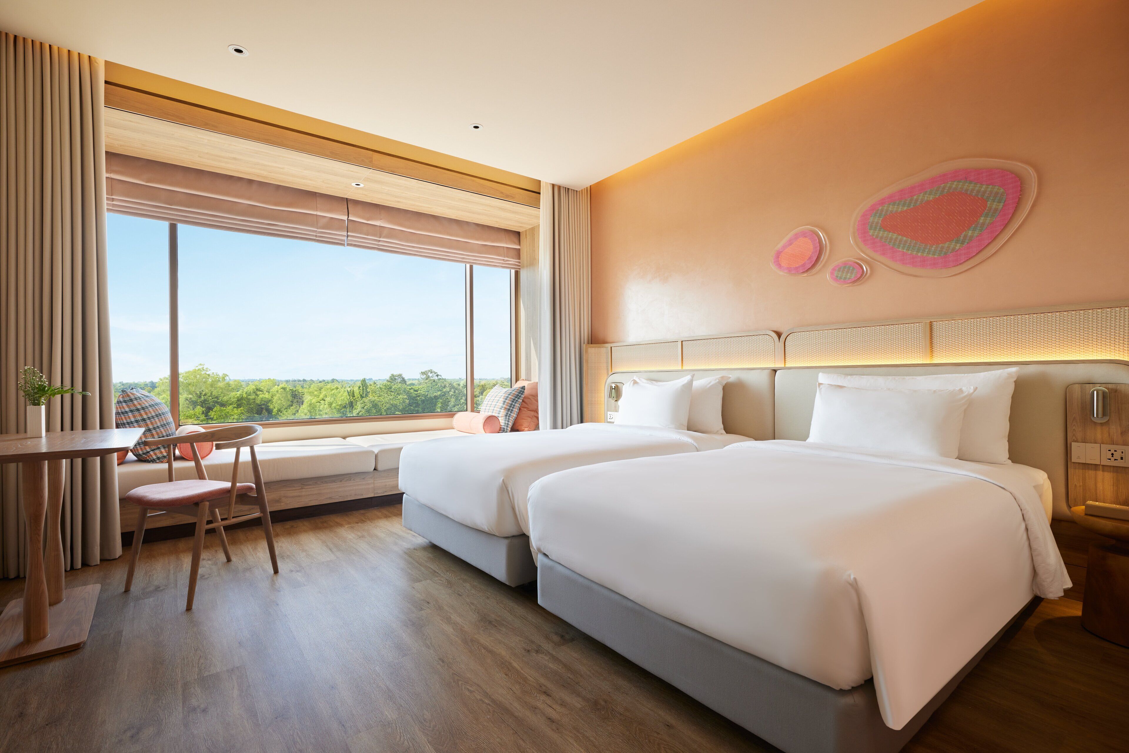 A hotel room with two beds, a dining table, and a large window offering a view of the outdoors.