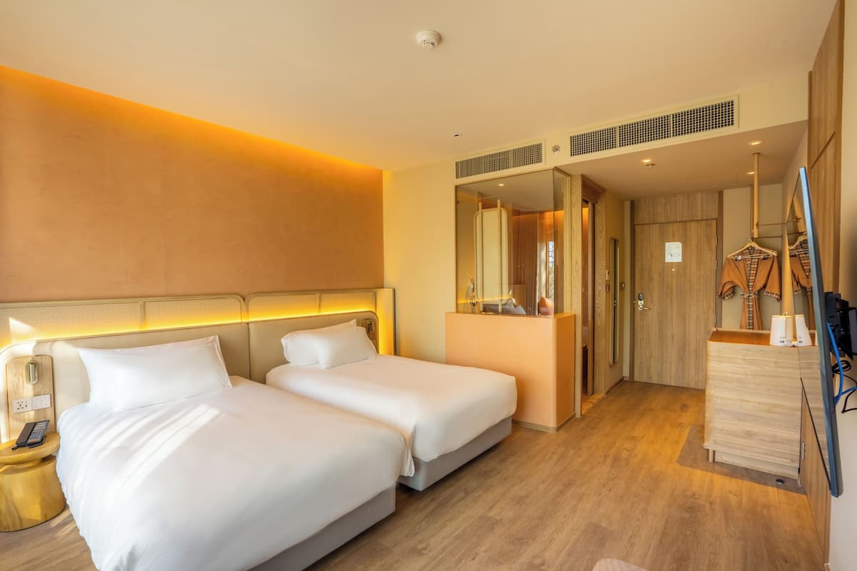 Habitación de hotel con dos camas, una mesita de noche con teléfono, un espejo, un aparador y un perchero.