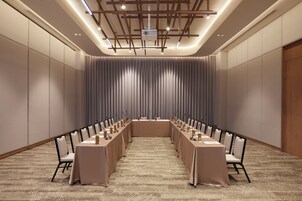 Un salón de conferencias con una larga mesa, sillas, un proyector y un fondo de cortina.