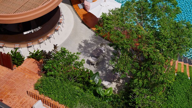 Uma área de piscina no terraço com espreguiçadeiras e guarda-sóis, cercada por vegetação e um caminho de tijolos.