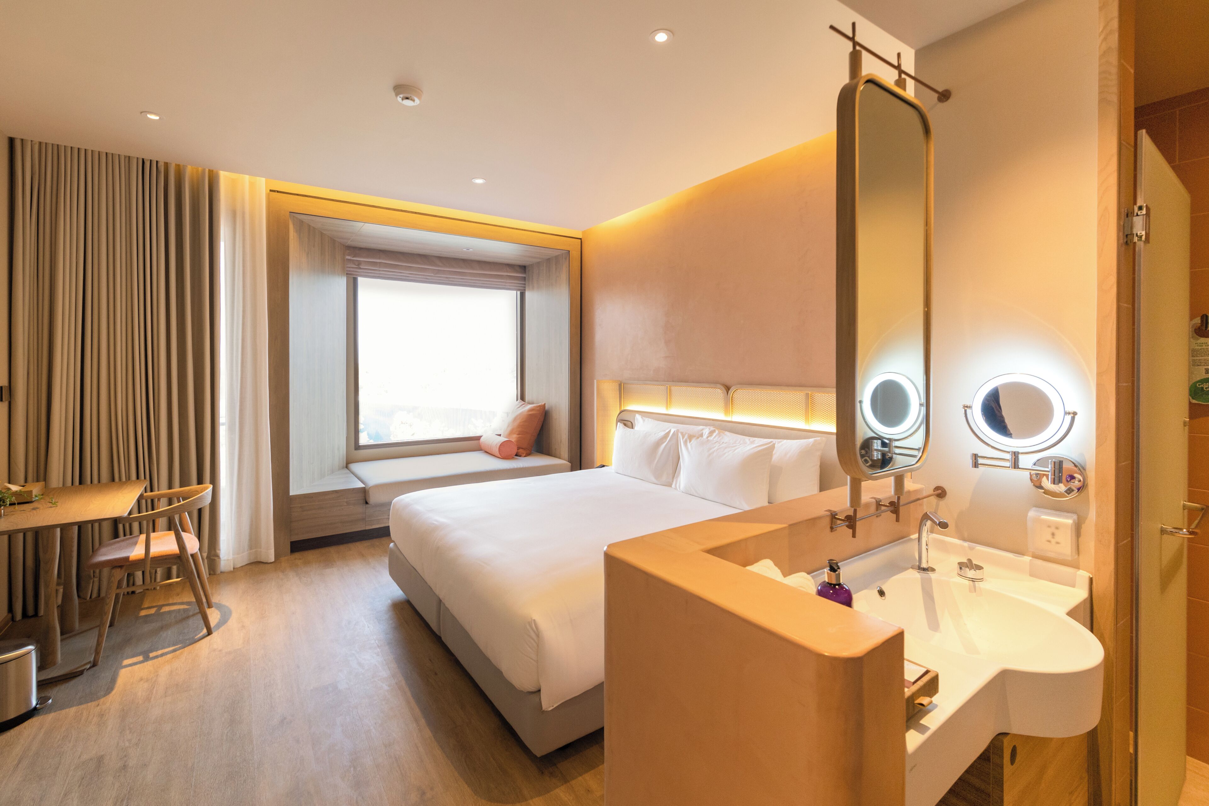 A hotel room with a bed, bedside table, mirror, and a window with curtains.