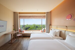 A hotel room with a large window, a bed, a sofa, a desk, and a TV.