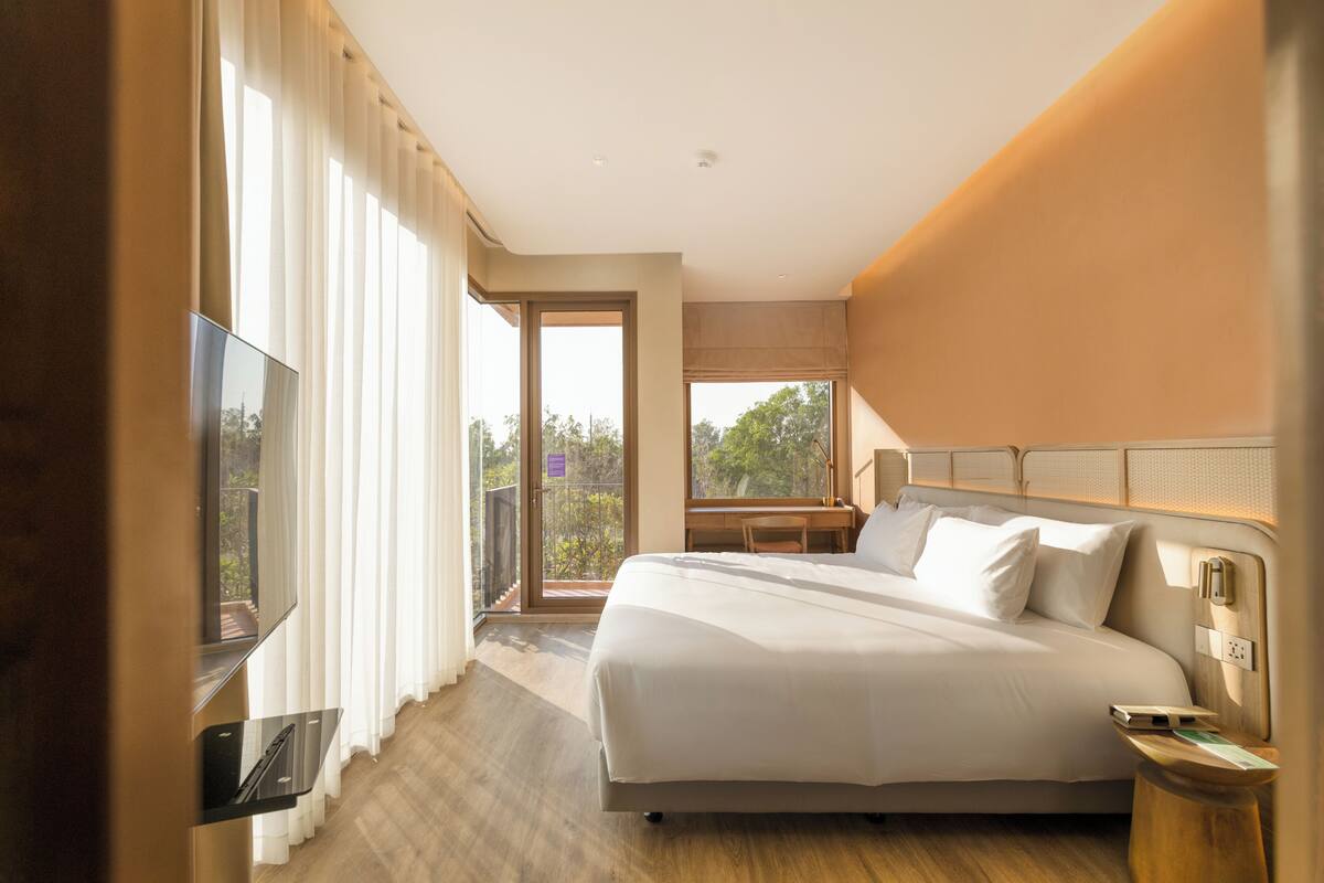 Habitación de hotel con cama, televisión, balcón y vistas, y suelo de madera.