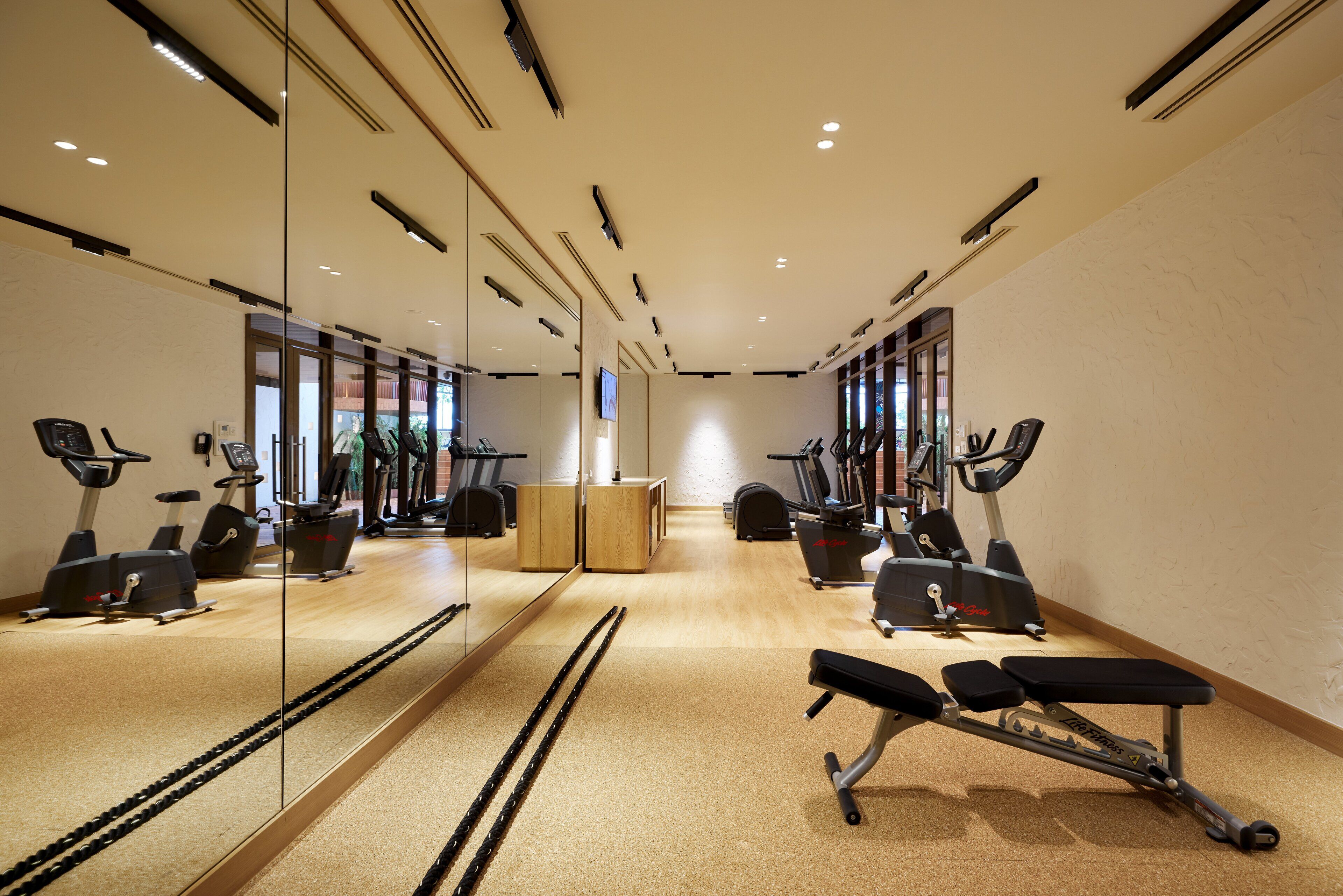 Une salle de sport équipée de matériel d’exercice, d’un banc et d’un mur recouvert de miroirs.