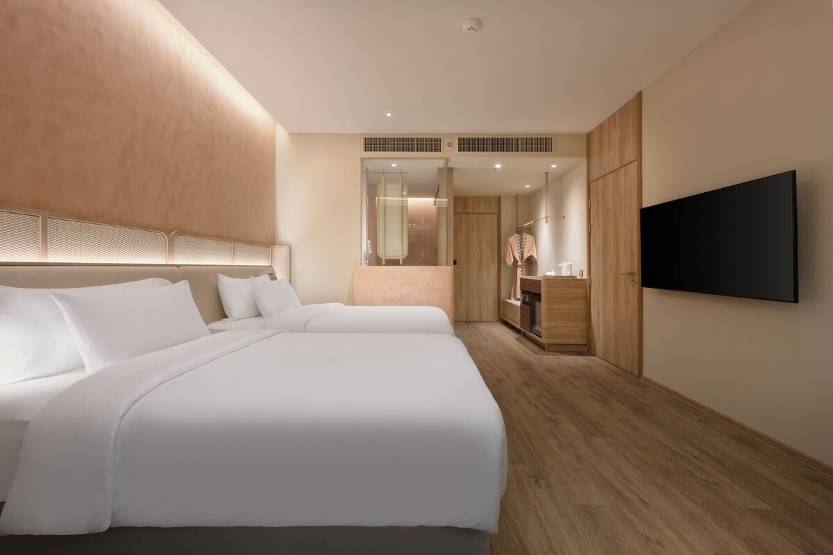 Habitación de hotel con dos camas, televisión, espejo y suelo de madera.