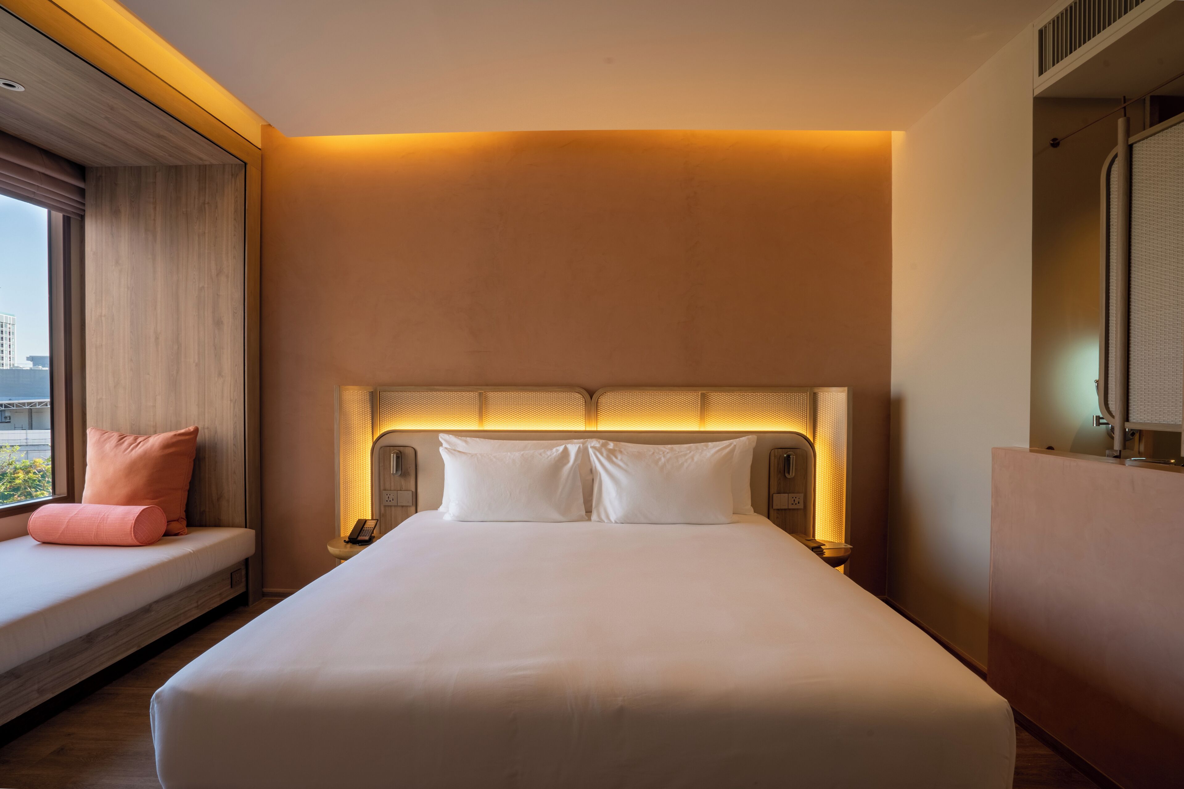 Een hotelkamer met een groot bed, nachtlampjes, een raam met uitzicht en een ingebouwde bank met kussens.