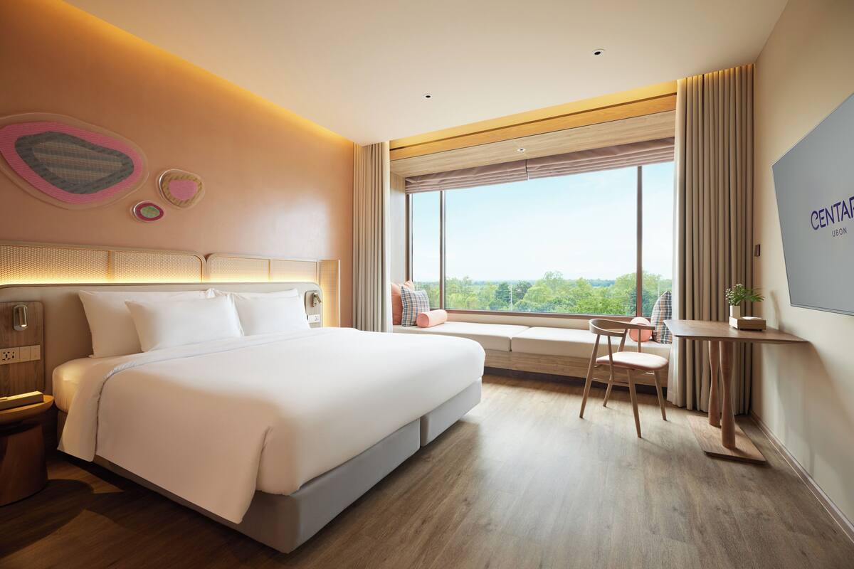 Una habitación de hotel moderna con una cama grande, un escritorio y un ventanal con vistas.