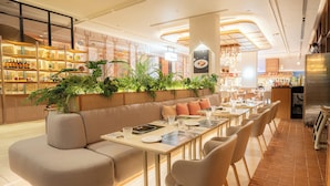 Um restaurante moderno com uma mesa de jantar comunitária alongada, assentos acolchoados e diversos vasos de plantas.