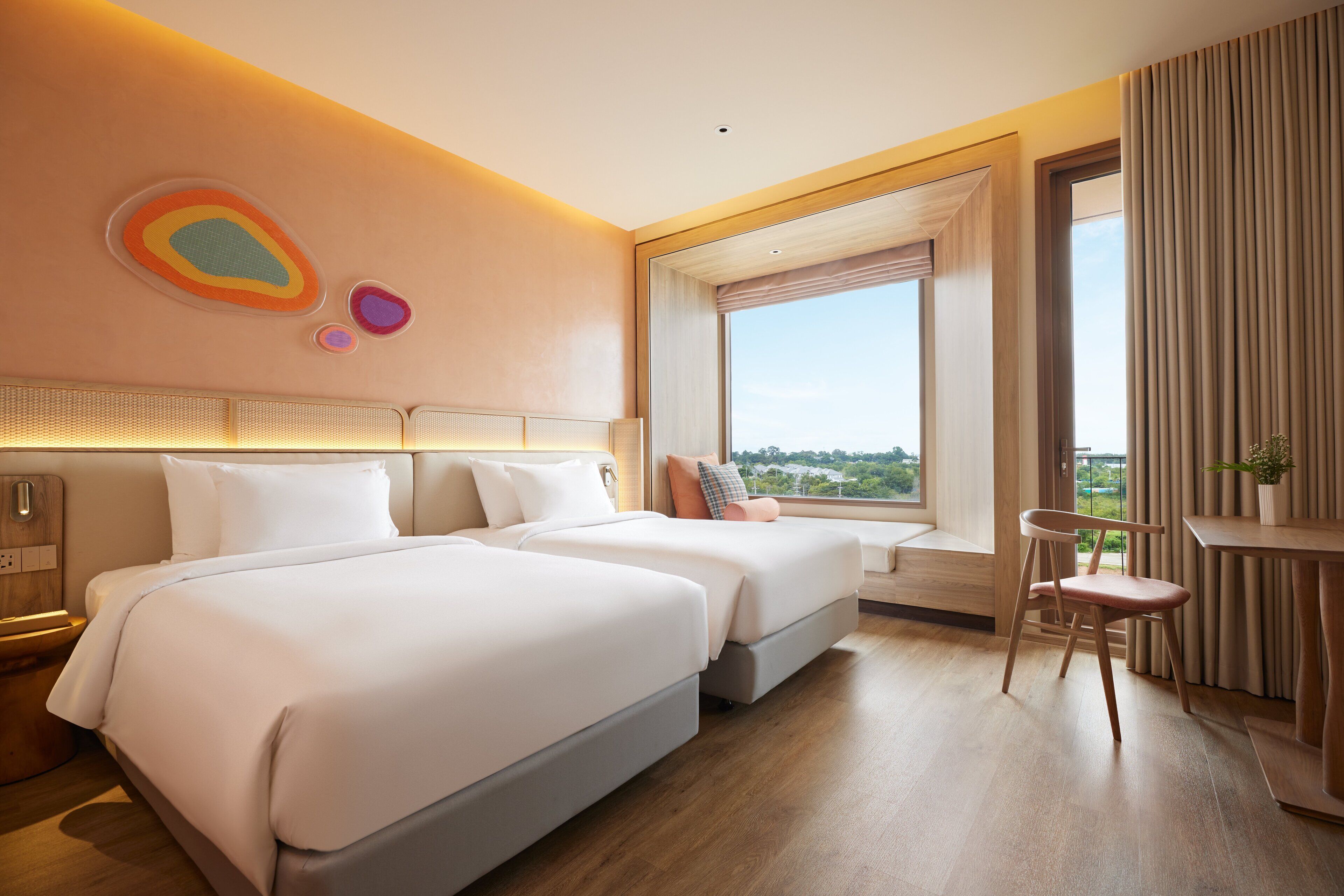 Habitación de hotel con dos camas, un escritorio, una silla y un ventanal con vistas.