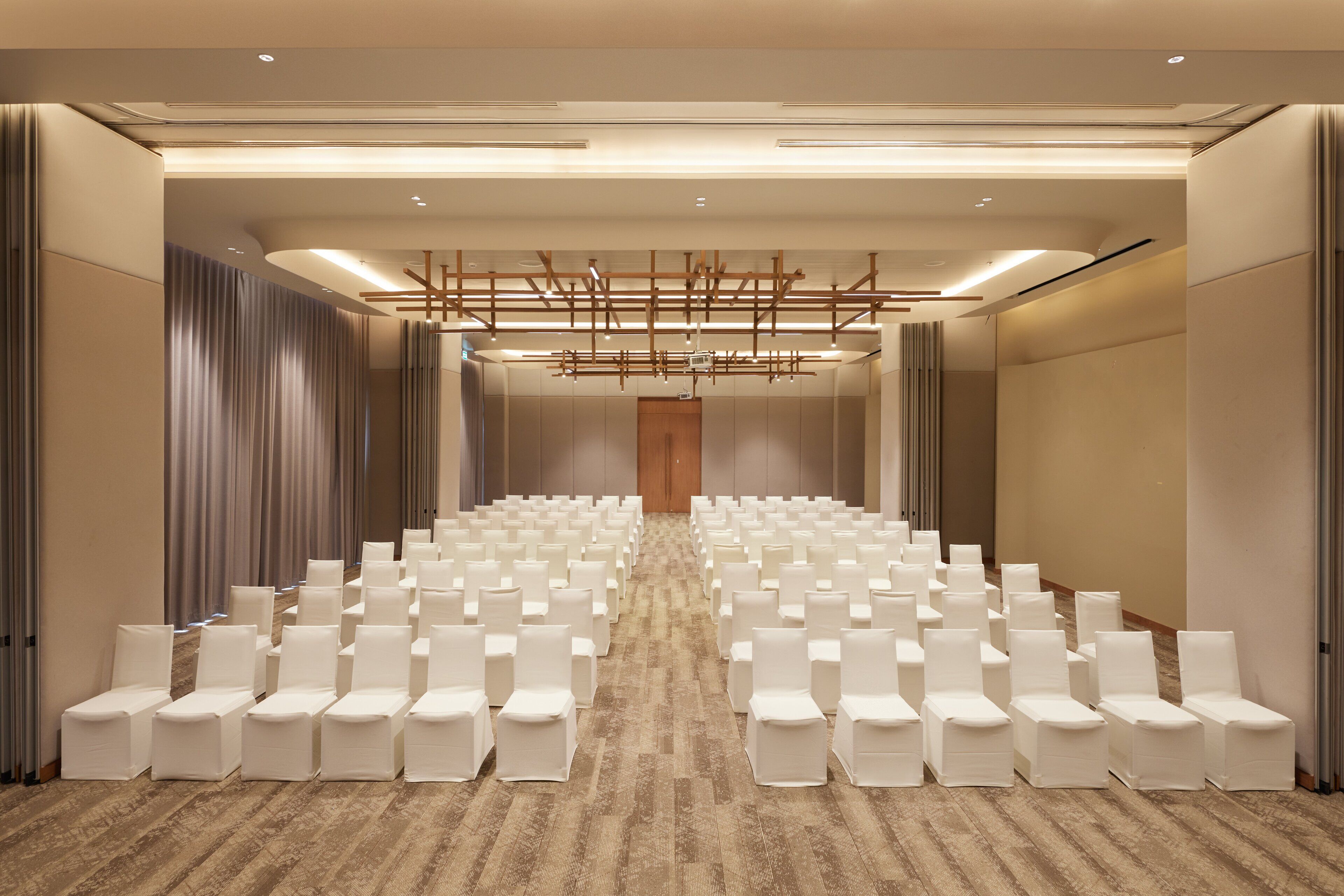 A conference room with rows of white chairs, a wooden door at the front, and a patterned carpet.