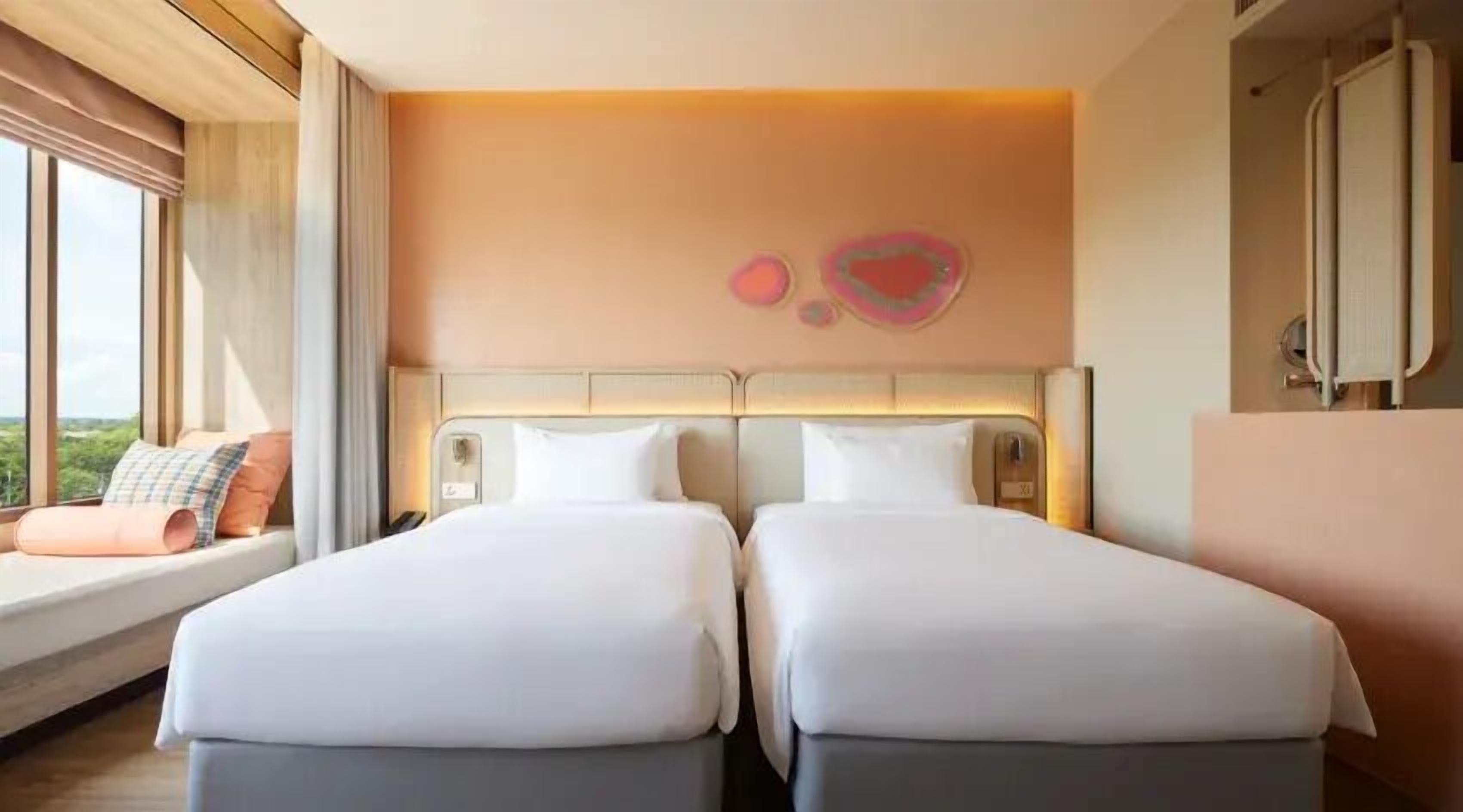 Una habitación de hotel con dos camas, un ventanal con vistas y un cabecero moderno.