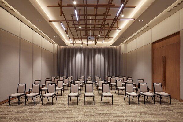 Un salón de conferencias con filas de sillas, techo de madera con iluminación y una puerta grande a la derecha.