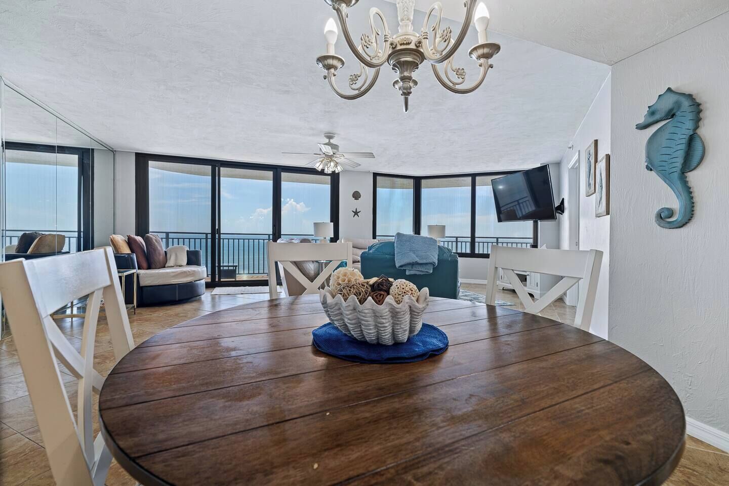 A spacious dining area with a round wooden table, white chairs, and a chandelier.