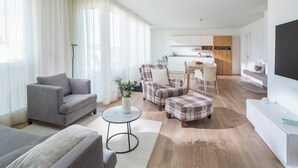 Uma sala de estar moderna com um sofá cinzento, uma poltrona xadrez e uma pequena mesa redonda com um vaso de flores.