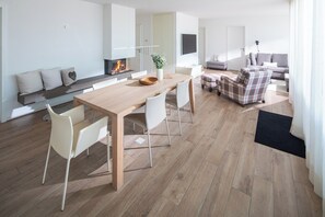 Een moderne woonkamer met een houten eettafel, witte stoelen, een geruit fauteuil en een open haard.