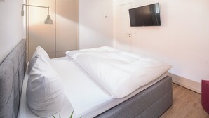 Cama bem arrumada com lençóis brancos, cabeceira cinza e abajur.