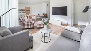 Uma sala de estar moderna com sofás cinzas, uma mesa de centro e uma TV fixada na parede.