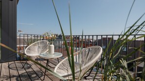 Terraço no telhado com duas cadeiras de vime branco e uma mesa pequena, delimitado por um guarda-corpo de metal.