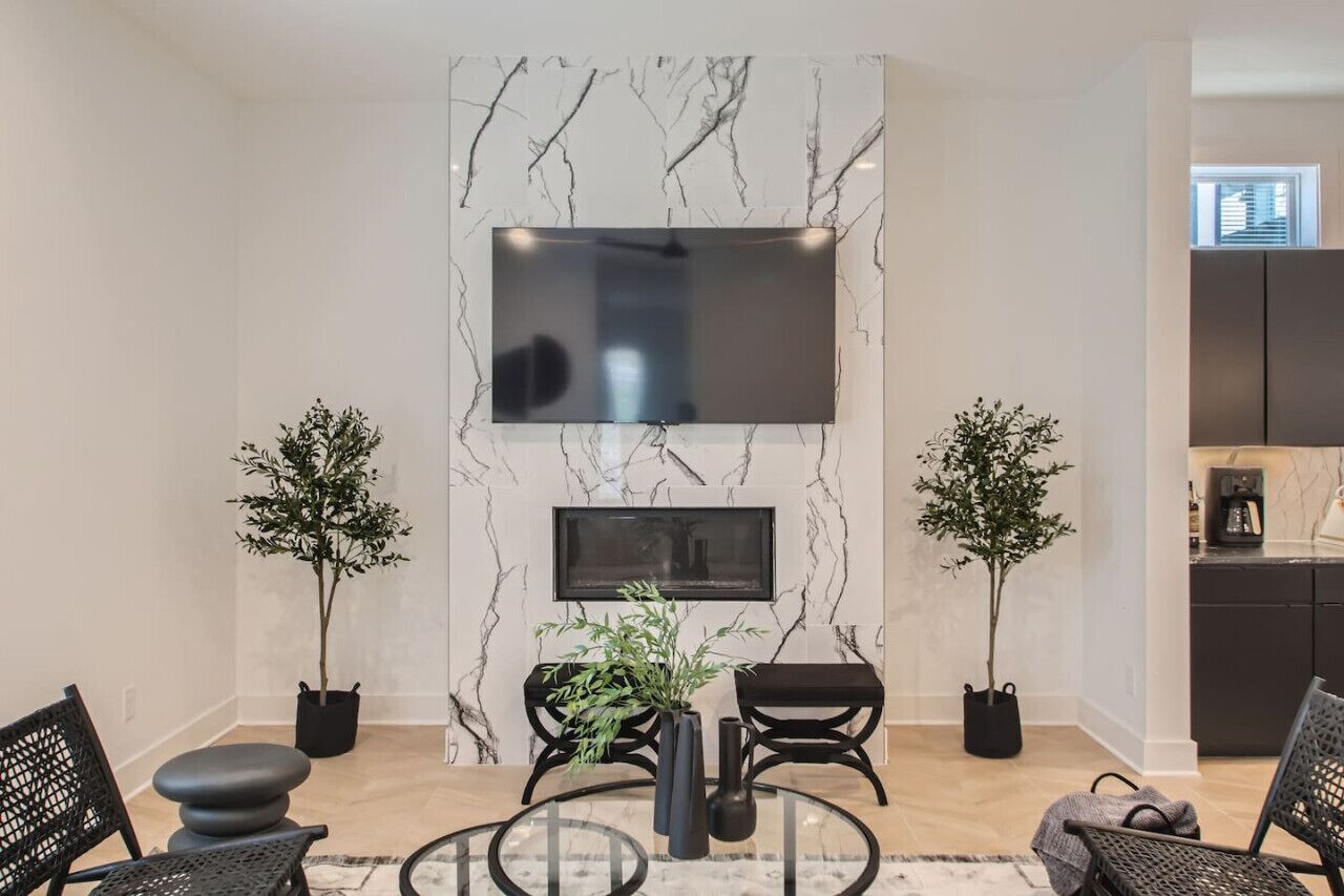 Una sala de estar moderna con una pared de mármol, un televisor de pantalla plana, dos plantas en macetas y una mesa de centro de cristal.