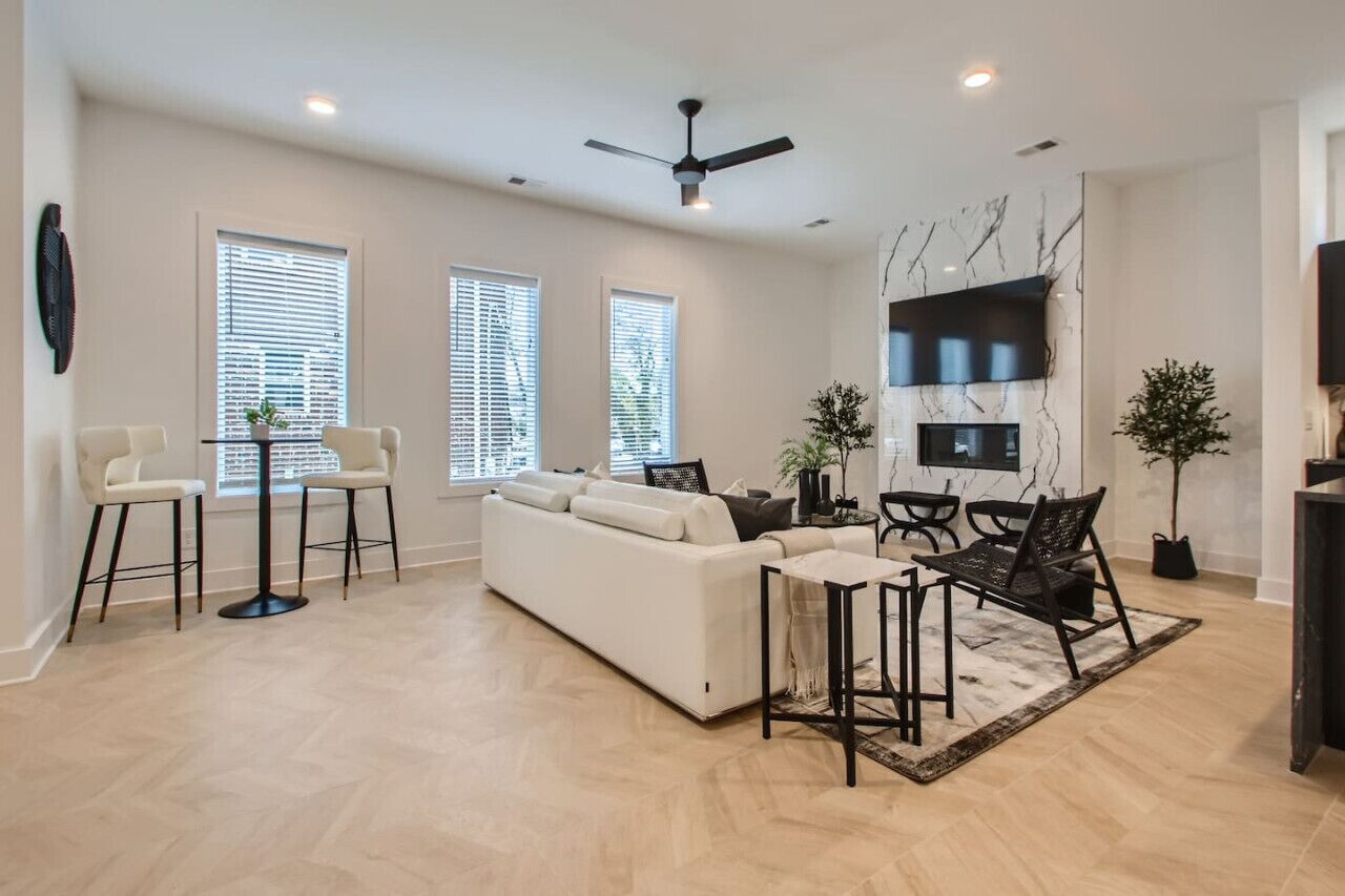 A spacious living room with a white sofa, two black chairs, a coffee table, and a ceiling fan.