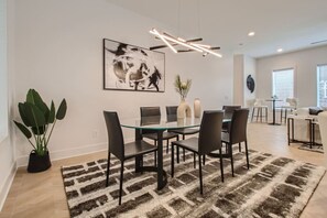 A modern dining area with a glass table, black chairs, a patterned rug, a large abstract painting, and a plant. - 4 - Music Row Modern - The Music City Collection (Nashville)