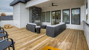 A modern outdoor patio with wooden flooring, grey wicker furniture, and a ceiling fan. - 4 - Music Row Modern - The Music City Collection (Nashville)