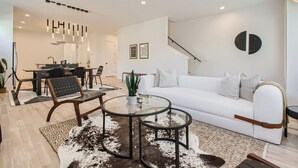 A modern living room with a white sofa, a glass coffee table, and a dining area with a black table and chairs. - 5 - Music Row Modern - The Music City Collection (Nashville)