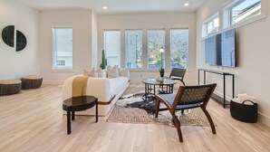 A spacious living room with a sofa, coffee table, and chairs, large windows, and a ceiling fan. - 5 - Music Row Modern - The Music City Collection (Nashville)