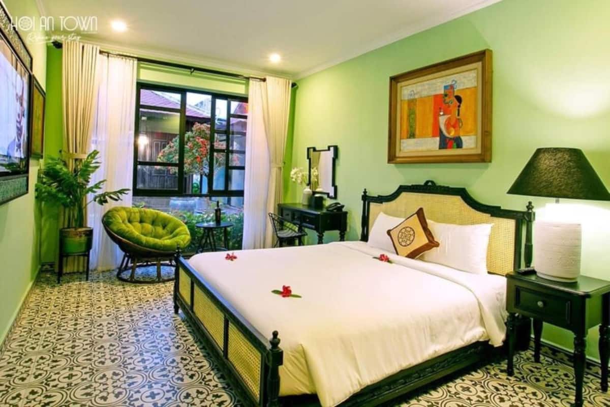 A hotel room with a bed, a chair, a table, a lamp, and a painting on the wall.
